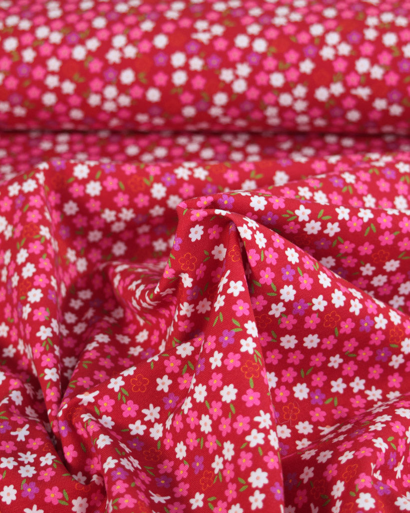 Red cotton jersey fabric with small pink and white daisy floral pattern