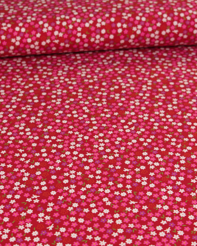 Red cotton jersey fabric with small ditsy daisy floral pattern