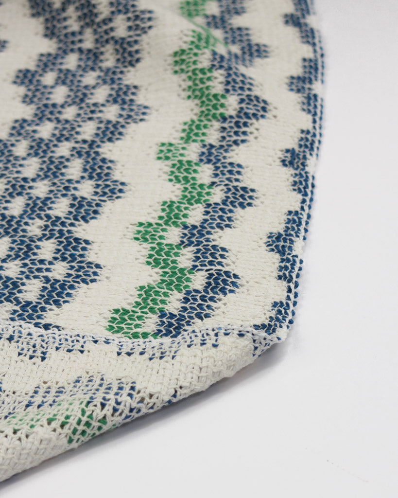 Close-up of a textured cotton knit fabric with blue and green pattern on a white background