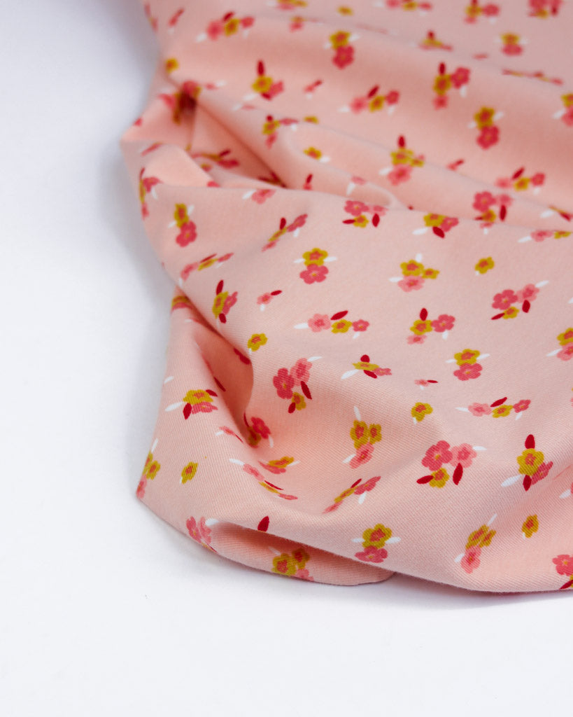 Pink cotton jersey fabric with small floral pattern on a white background