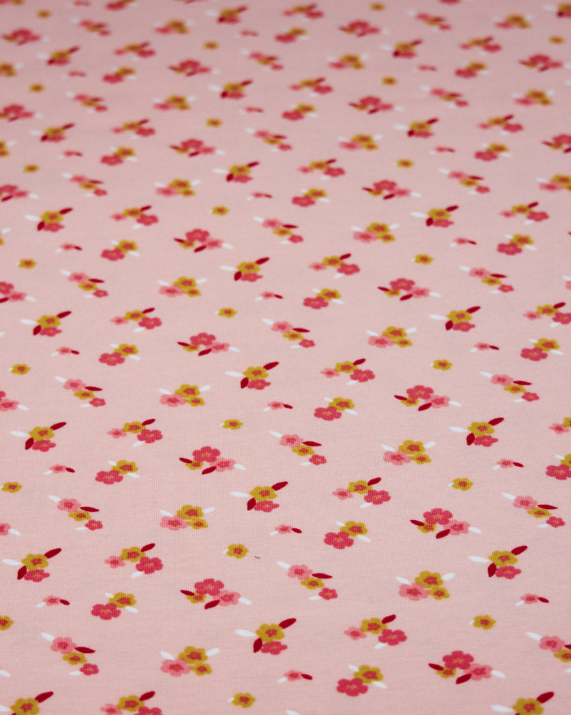 Ditsy floral pattern cotton jersey fabric on a pale pink background