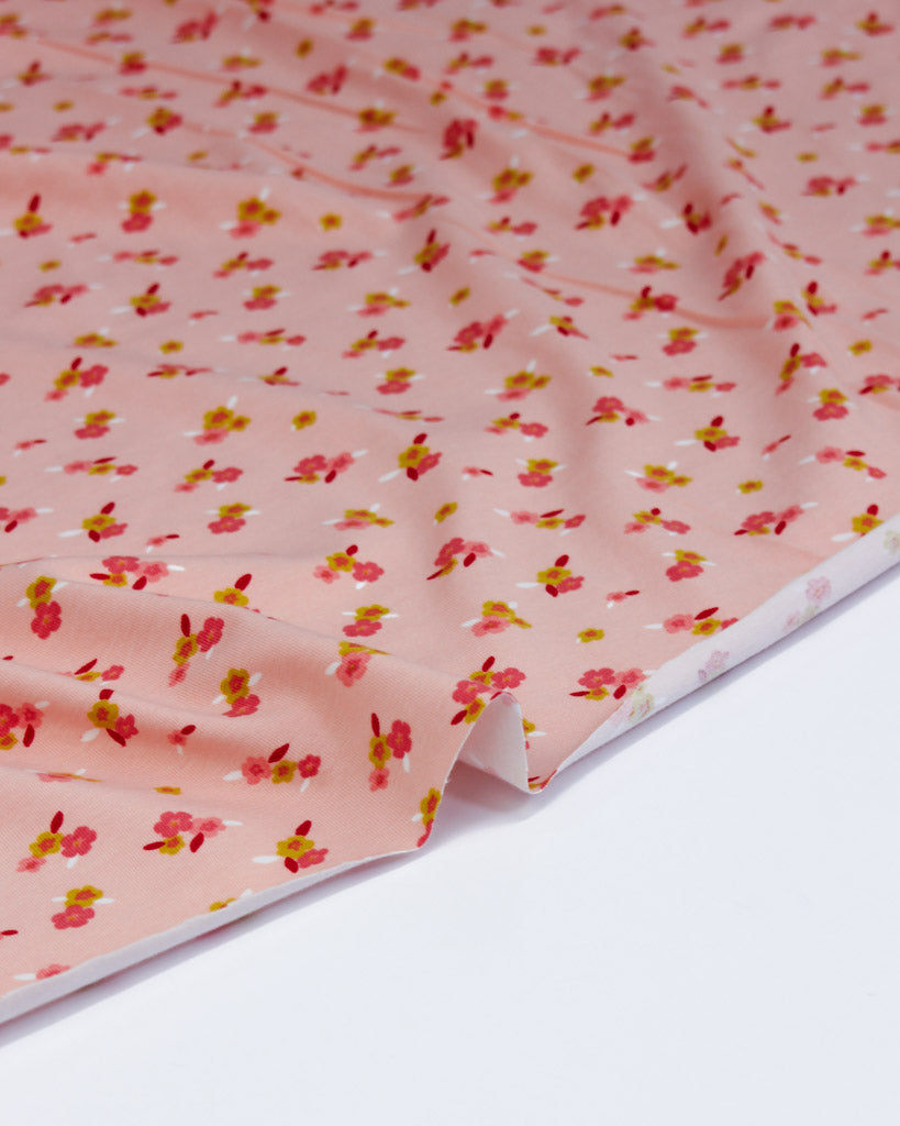 Ditsy floral-patterned cotton jersey fabric on a pale pink background