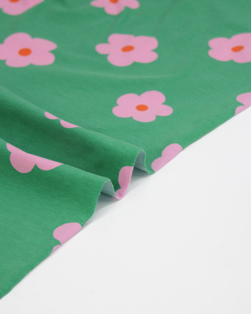 Green jersey knit fabric with pink  daisy flowers on a white background