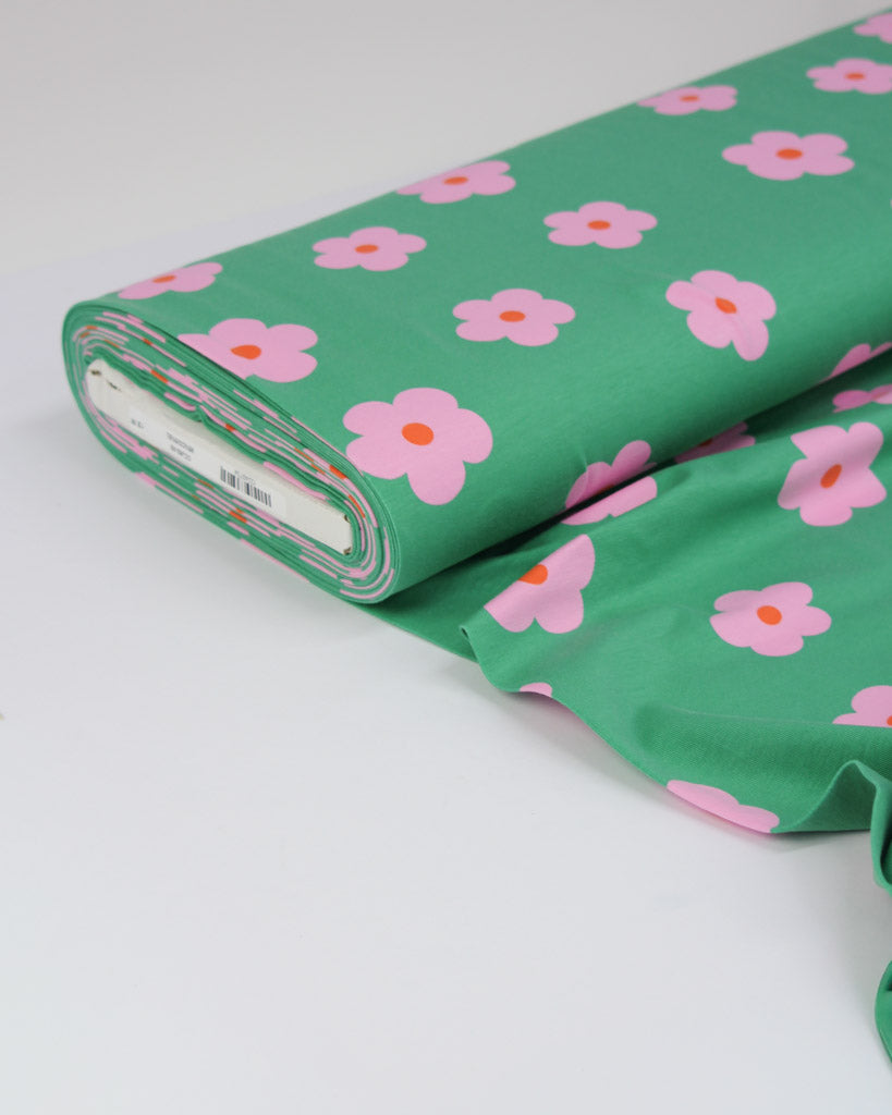 Roll of green cotton jersey fabric with pink floral pattern on a white background