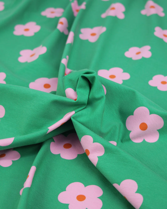 Close-up of green jersey fabric with pink daisy floral patterns