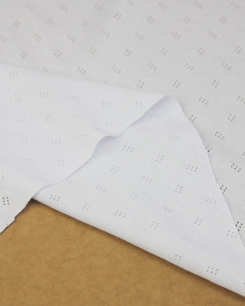 White pointelle jersey knit fabric on brown surface