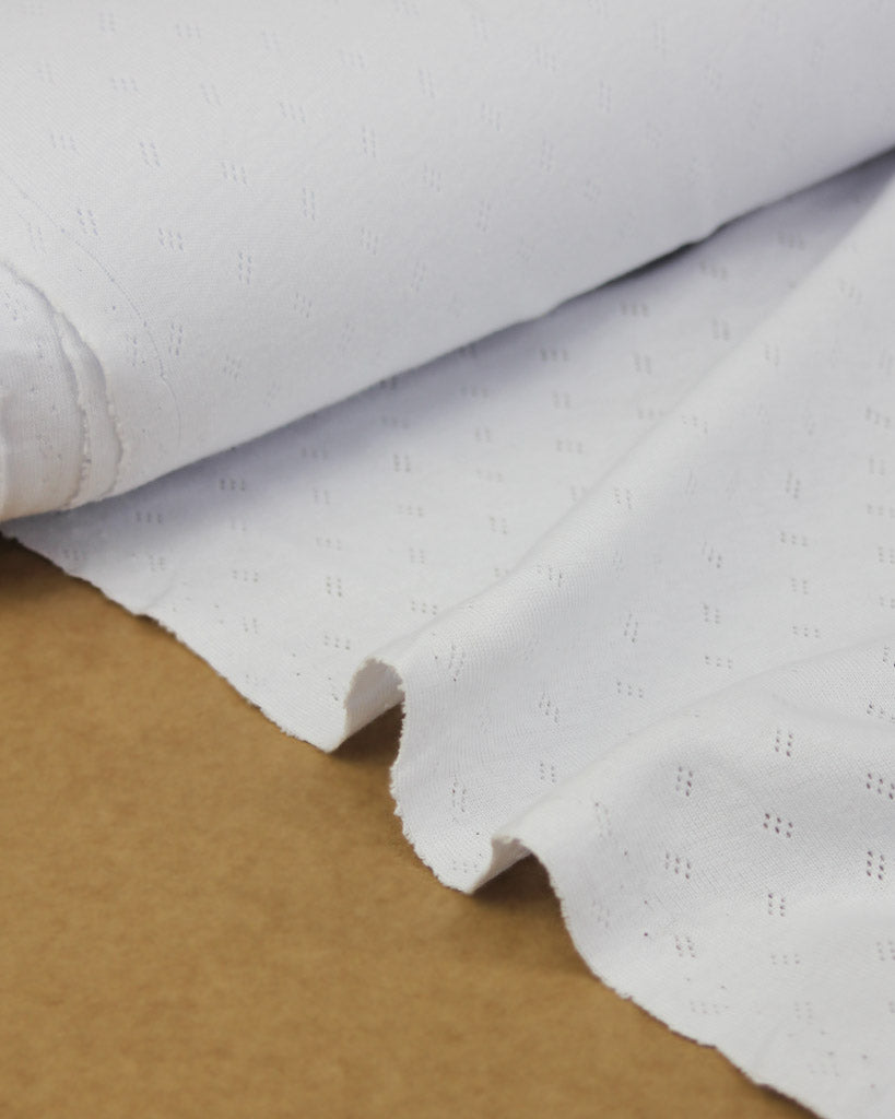 Close-up of white pointelle fabric with a textured pattern on a brown surface