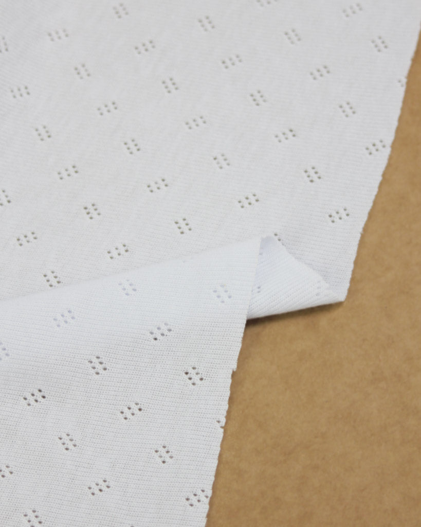 White pointelle jersey fabric on a brown surface