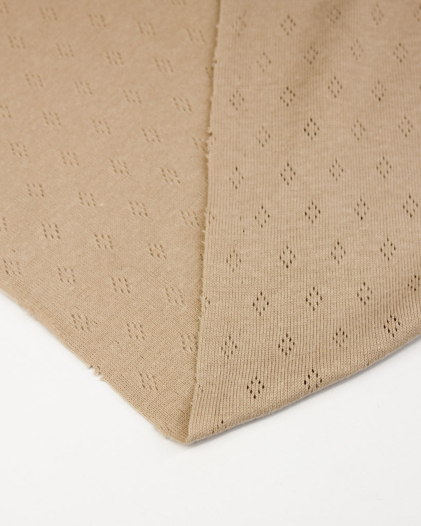Beige pointelle fabric with a subtle pattern on a white background