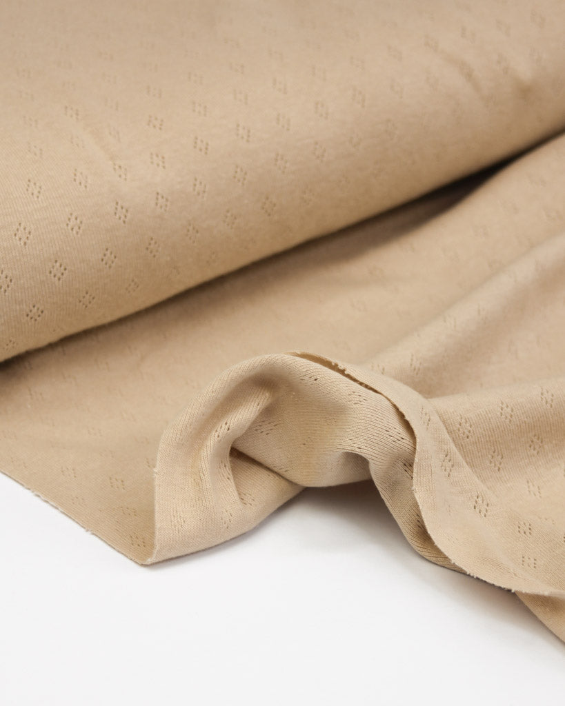 Close-up of beige textured pointelle fabric on a white background