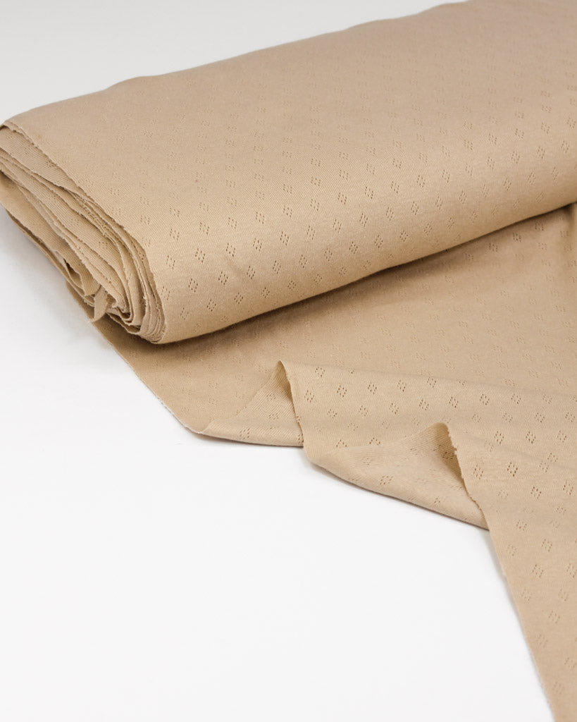 Folded beige pointelle fabric with a subtle pattern on a white background