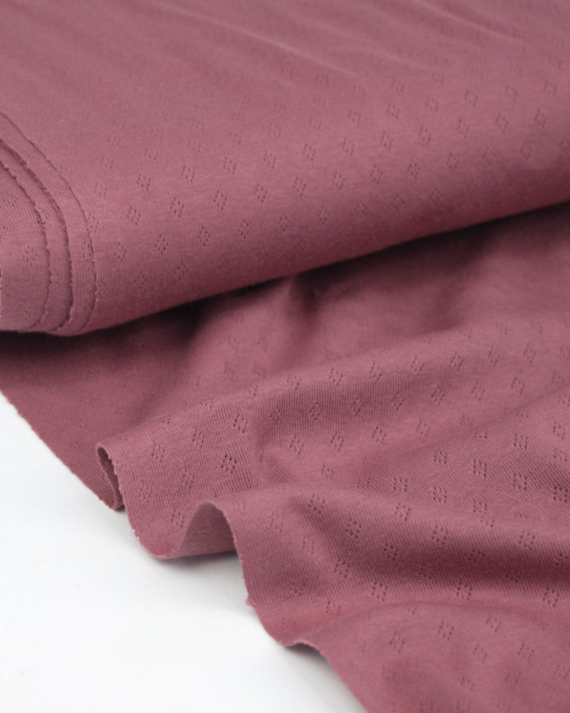 Close-up of a textured mulberry pink pointelle fabric with a subtle pattern on a white background
