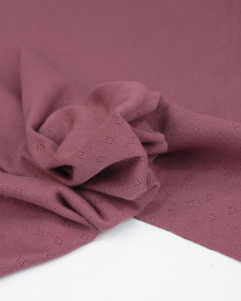 Close-up of a folded mulberry pointelle fabric with a textured pattern on a white background