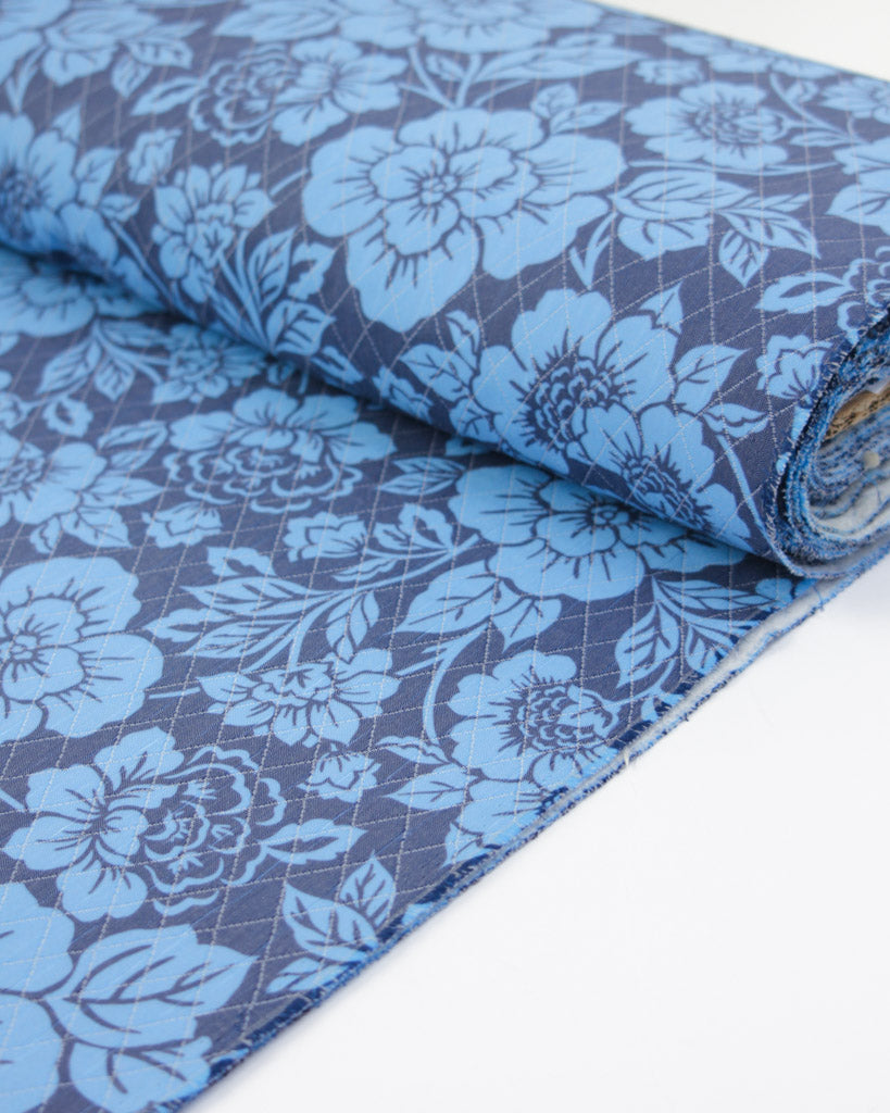 Roll of blue floral quilted fabric on a white background