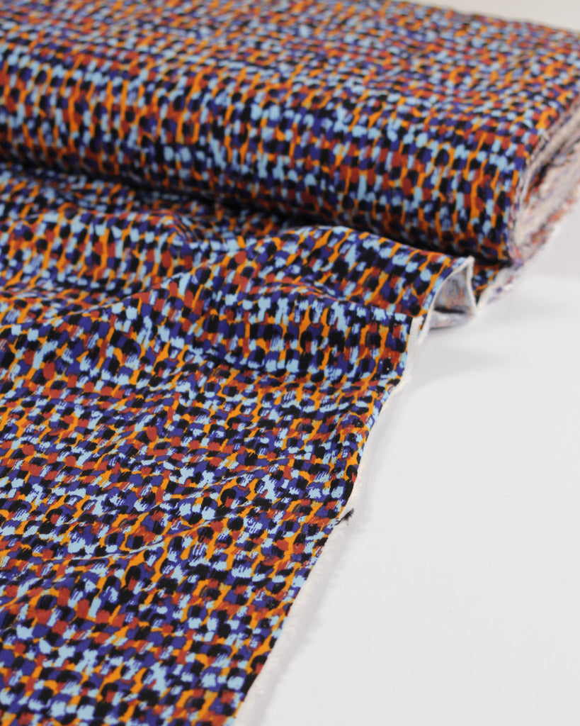 Patterned viscose twill fabric with blue and orange dot design on a white background