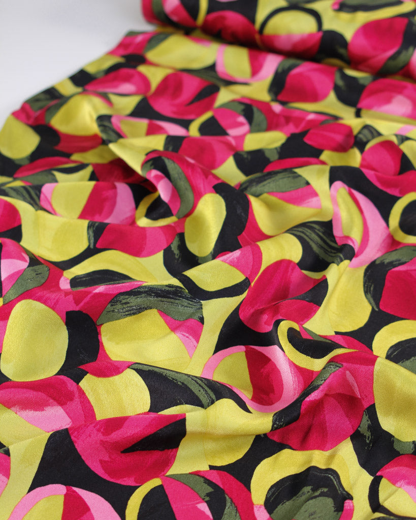 Colourful viscose satin fabric with abstract pattern in hot pink, black and chartreuse on a white background