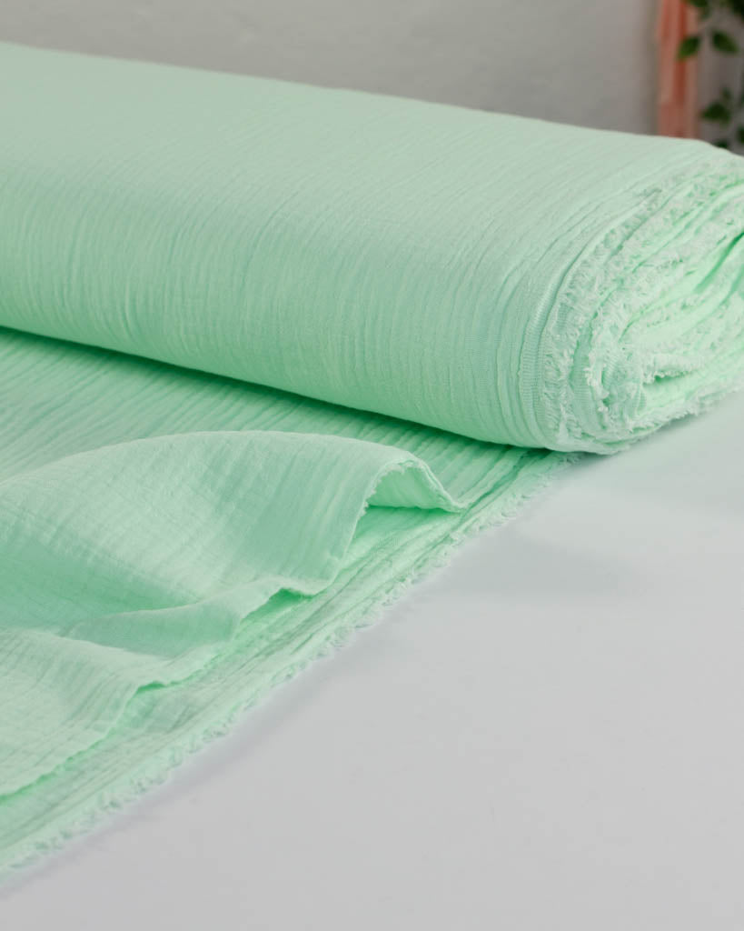 Roll of pastel mint green cotton double gauze fabric on a white surface