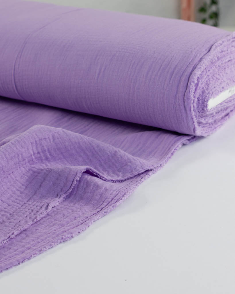 Roll of pale purple cotton double gauze fabric on a white surface