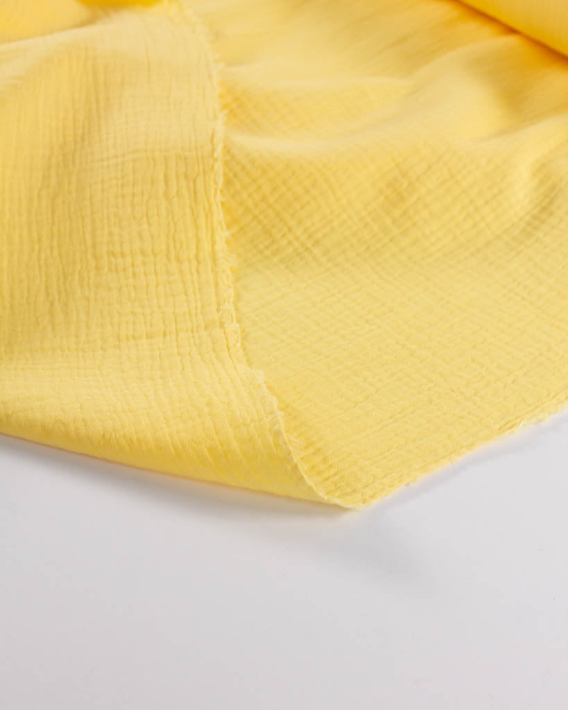 Close-up of banana yellow textured cotton double gauze fabric on a white background
