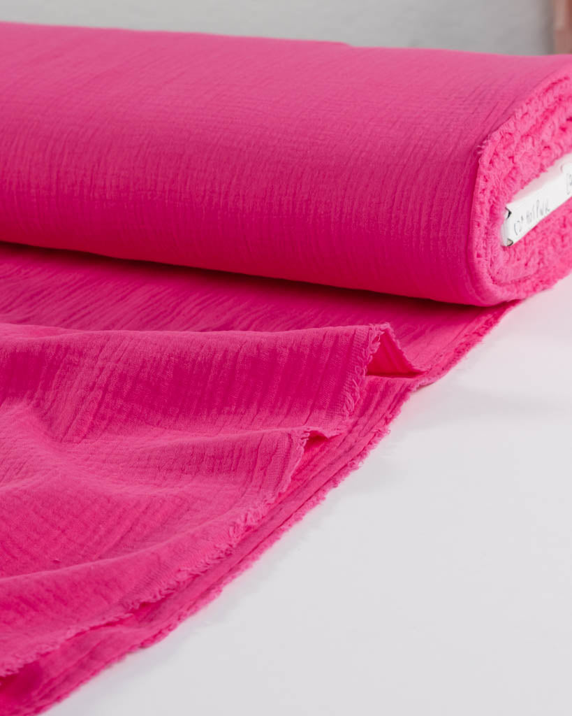 Roll of hot pink cotton double gauze fabric on a white background