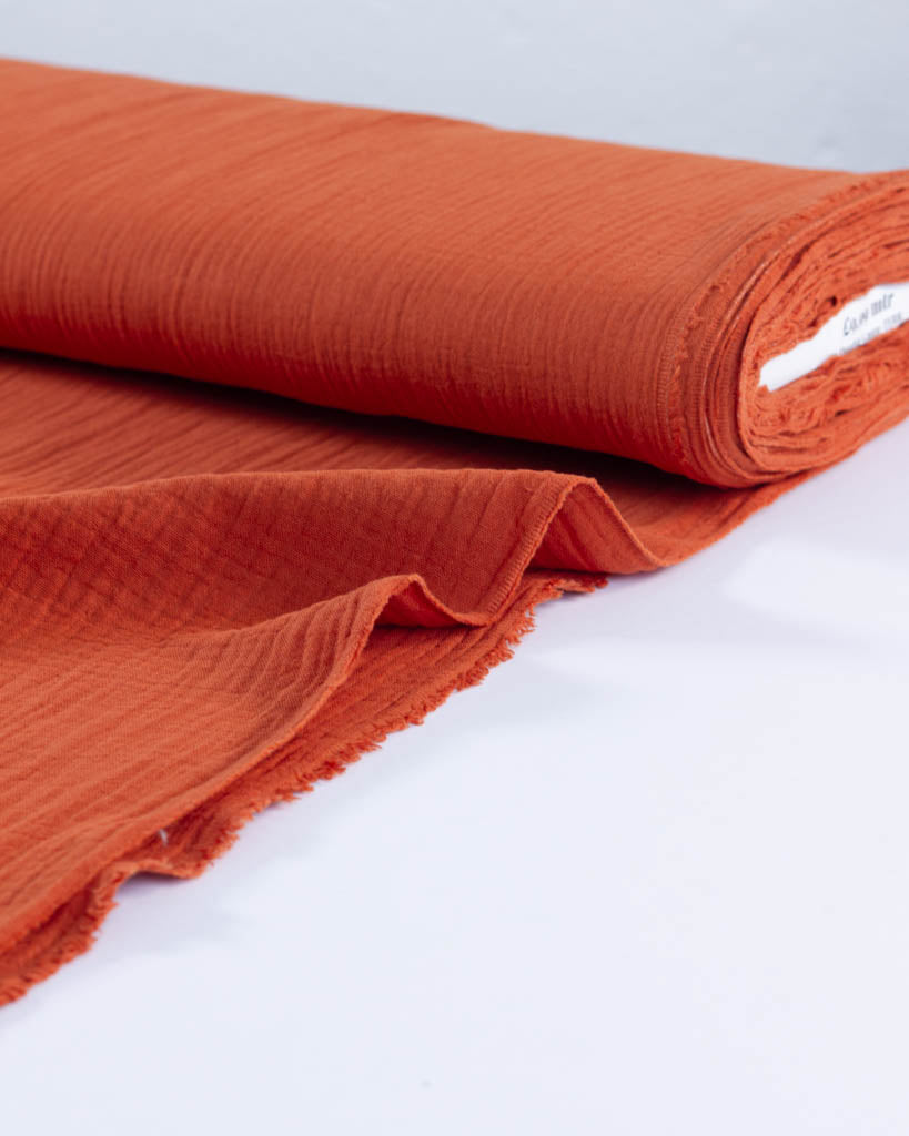 Roll of orange cotton double gauze fabric on a white background