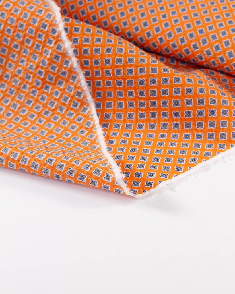 Reverse view of mango orange cotton seersucker fabric with small four-petal floral tile print