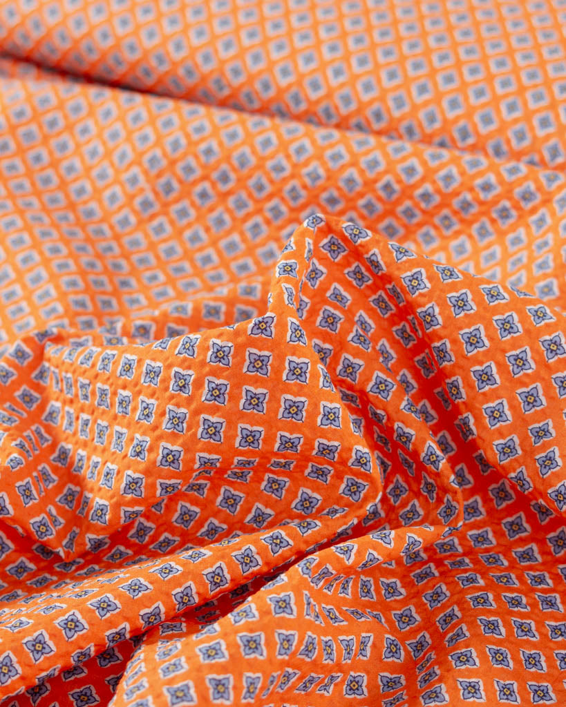 Close-up of mango orange cotton seersucker fabric with small four-petal floral tile print