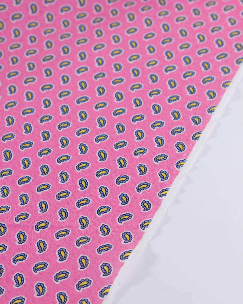 Selvedge edge of 100% cotton seersucker fabric in bubblegum pink with a tiny blue & yellow paisley print