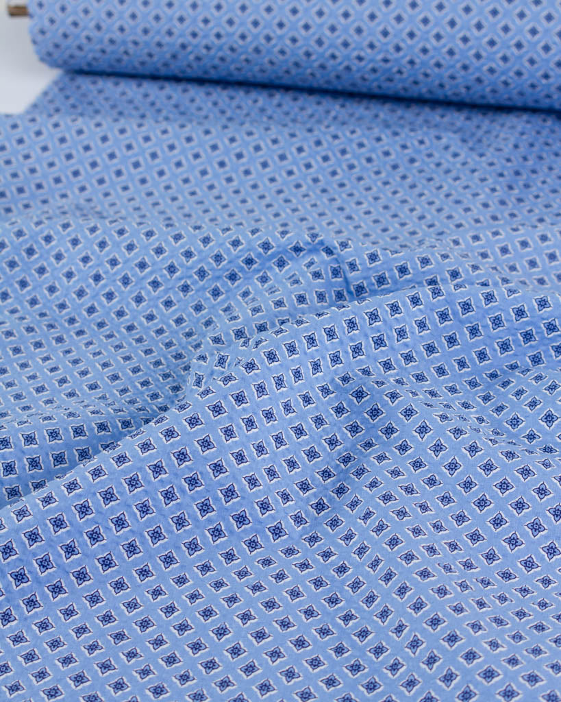 Roll of textured sky blue cotton fabric with an all-over four-petal flower motif