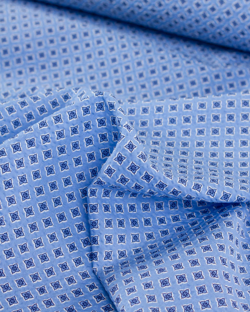 Sky blue cotton seersucker fabric with small four-petal floral tile print
