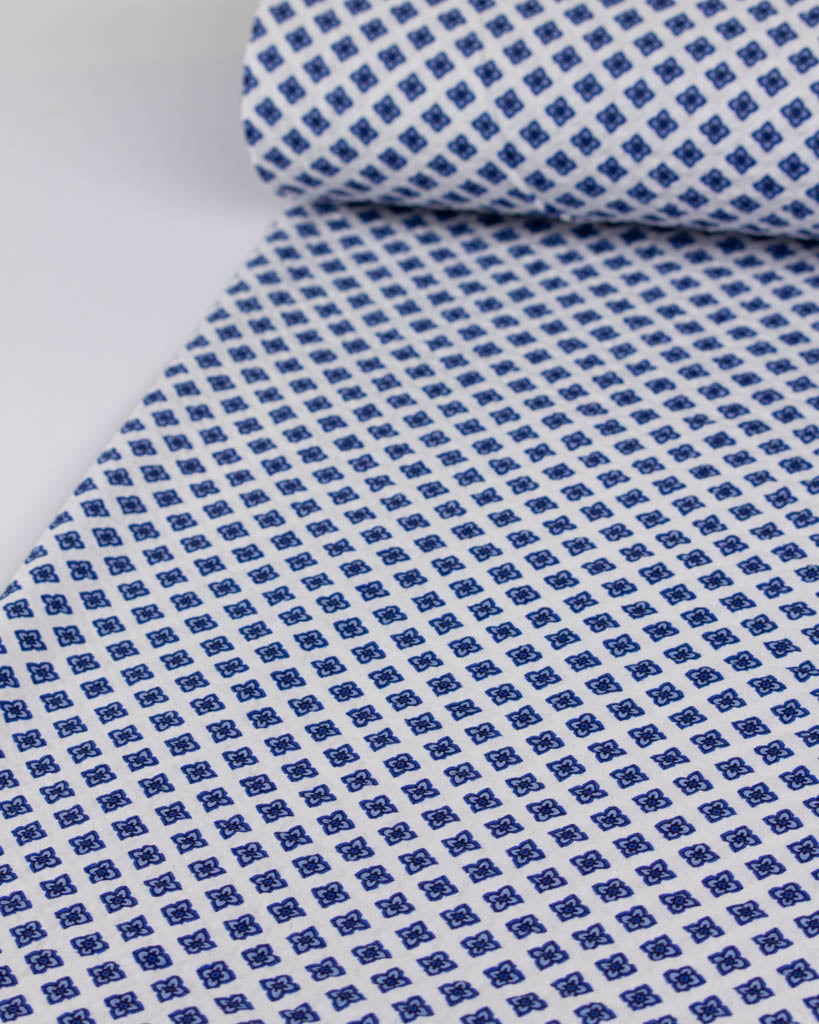 Roll of textured white cotton fabric with an all-over four-petal geometric flower pattern