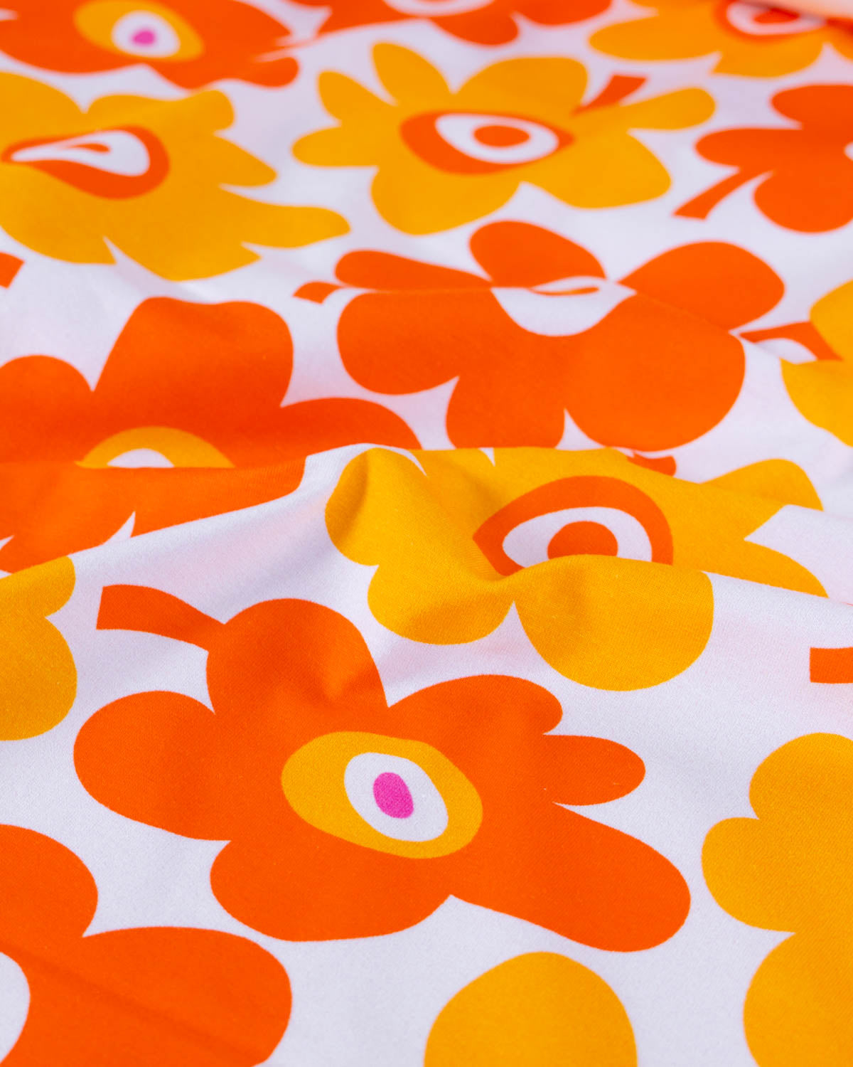 Cotton jersey fabric with a pattern of orange and yellow graphic flowers on a white background
