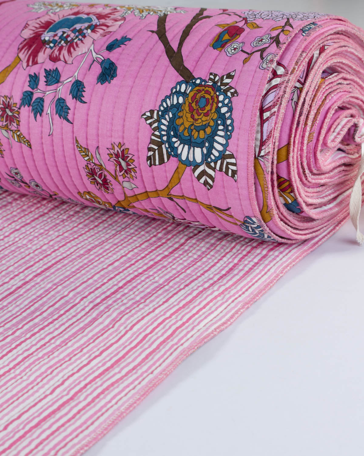 Roll of pink cotton quilted fabric with colorful floral patterns on a white background