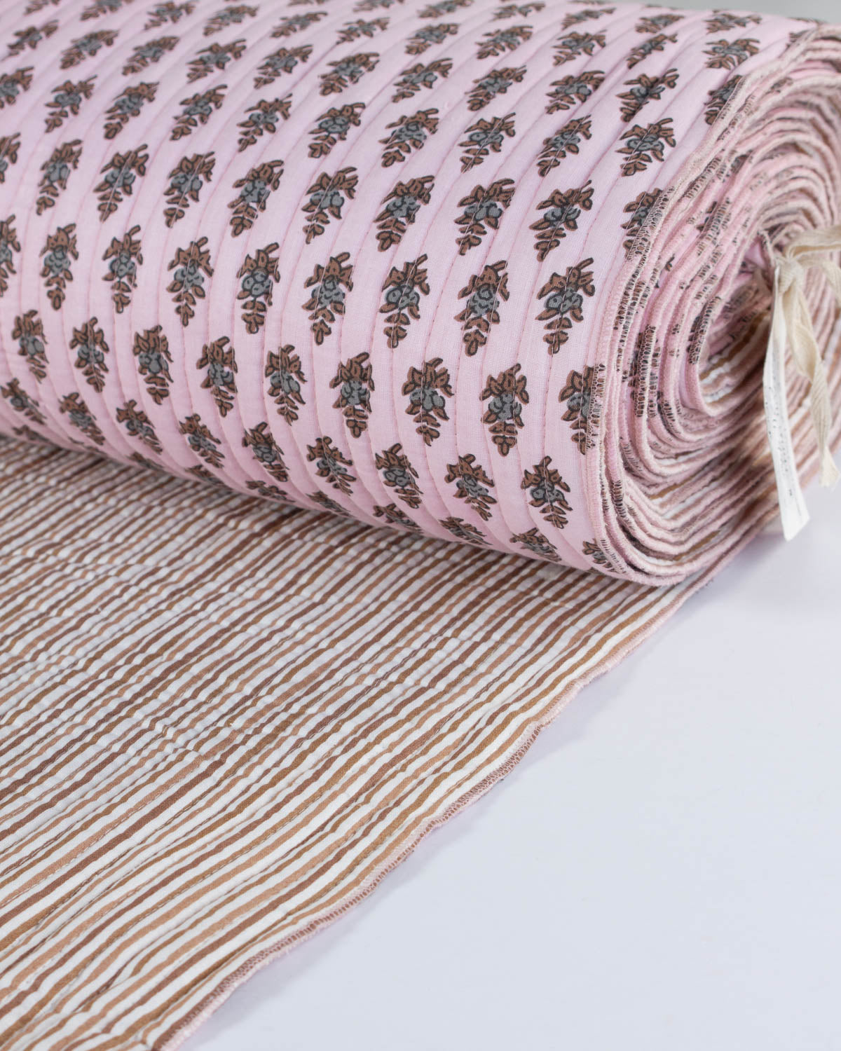 Roll of pink quilted cotton fabric with a floral pattern on a white background