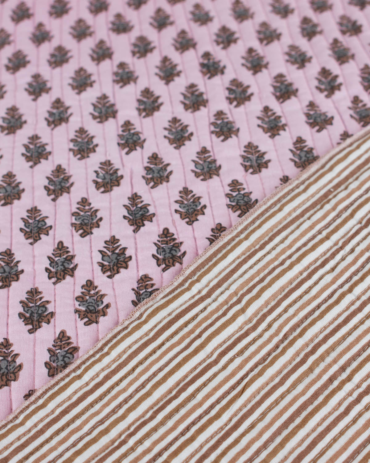 Close-up of pink quilted cotton fabric with leaf pattern and brown striped fabric