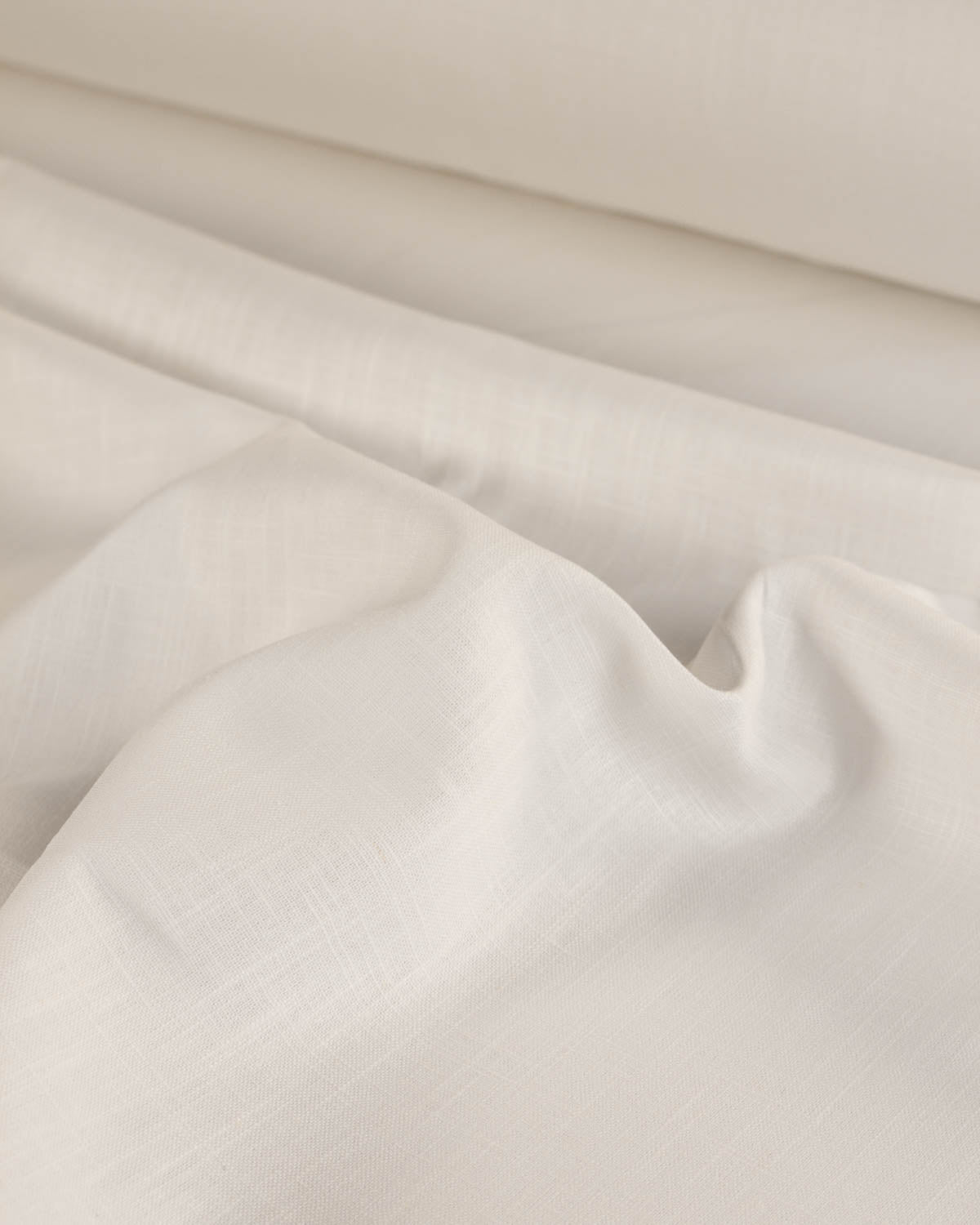 A close-up of draped cream-colored washed linen fabric with a soft, textured weave and gentle folds.