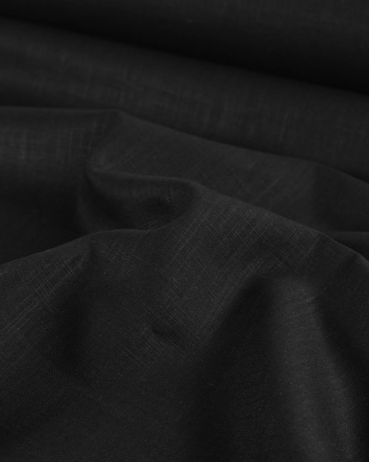 A close-up of black washed linen fabric with a subtle woven texture, shown in soft folds.