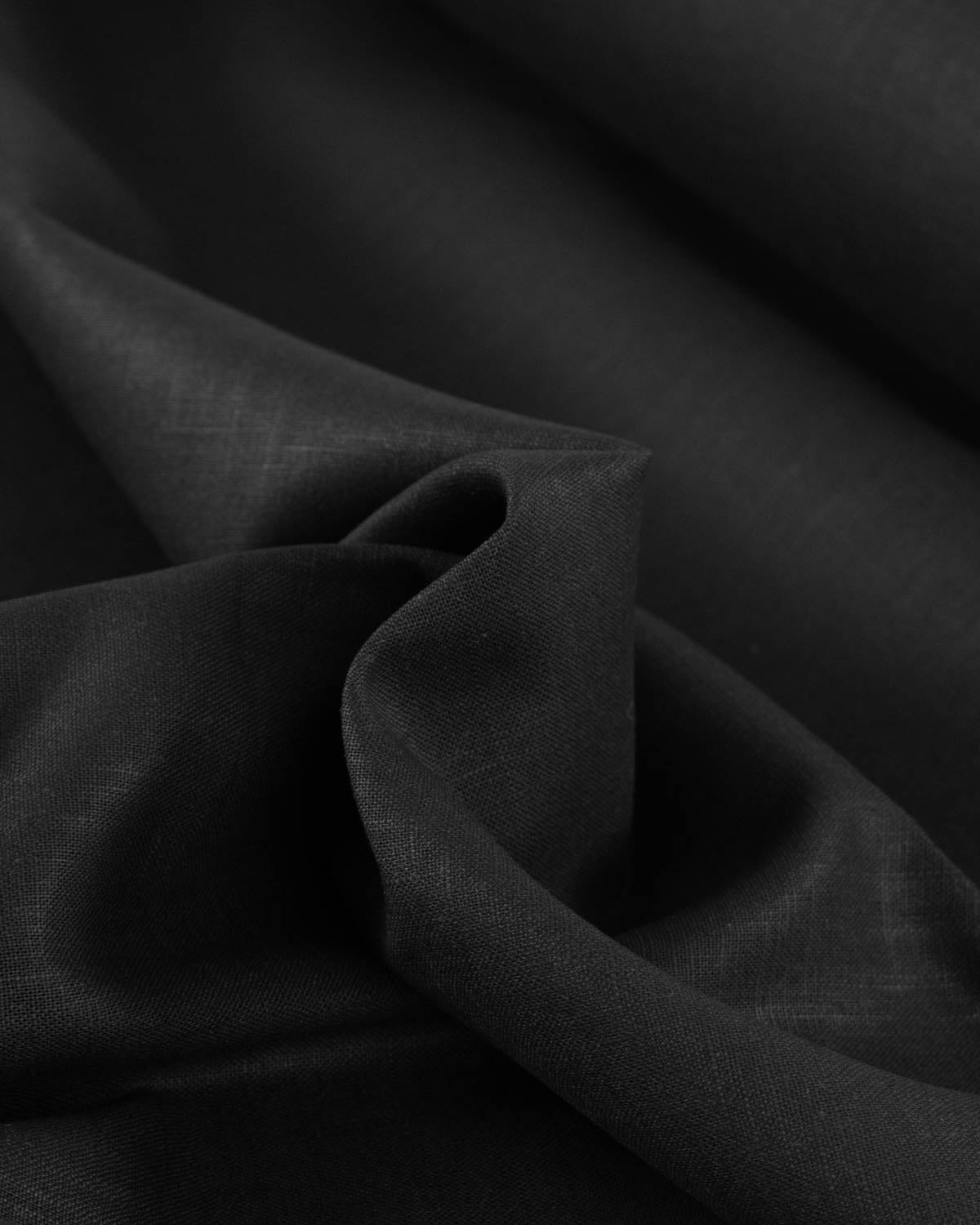 A close-up of draped black washed linen fabric with soft folds and a subtle woven texture.