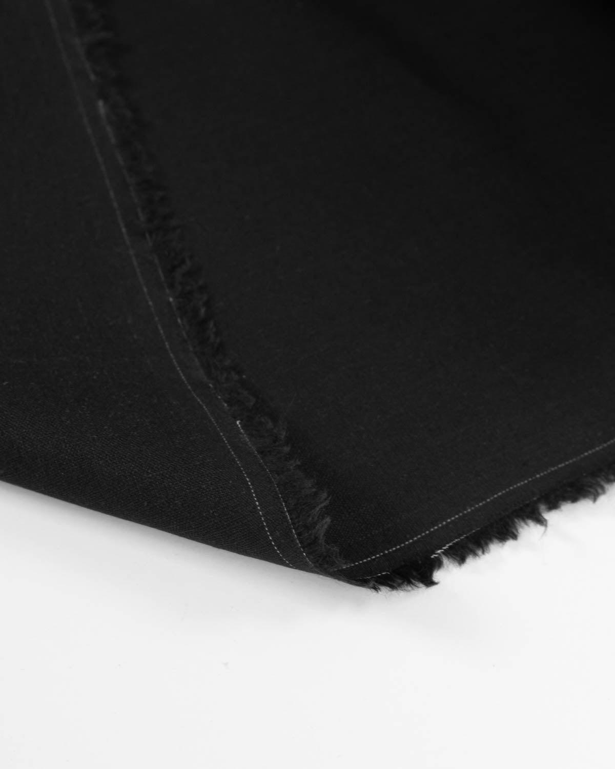 Close-up of black linen  fabric with a raw, frayed hem edge folded over on a white surface.
