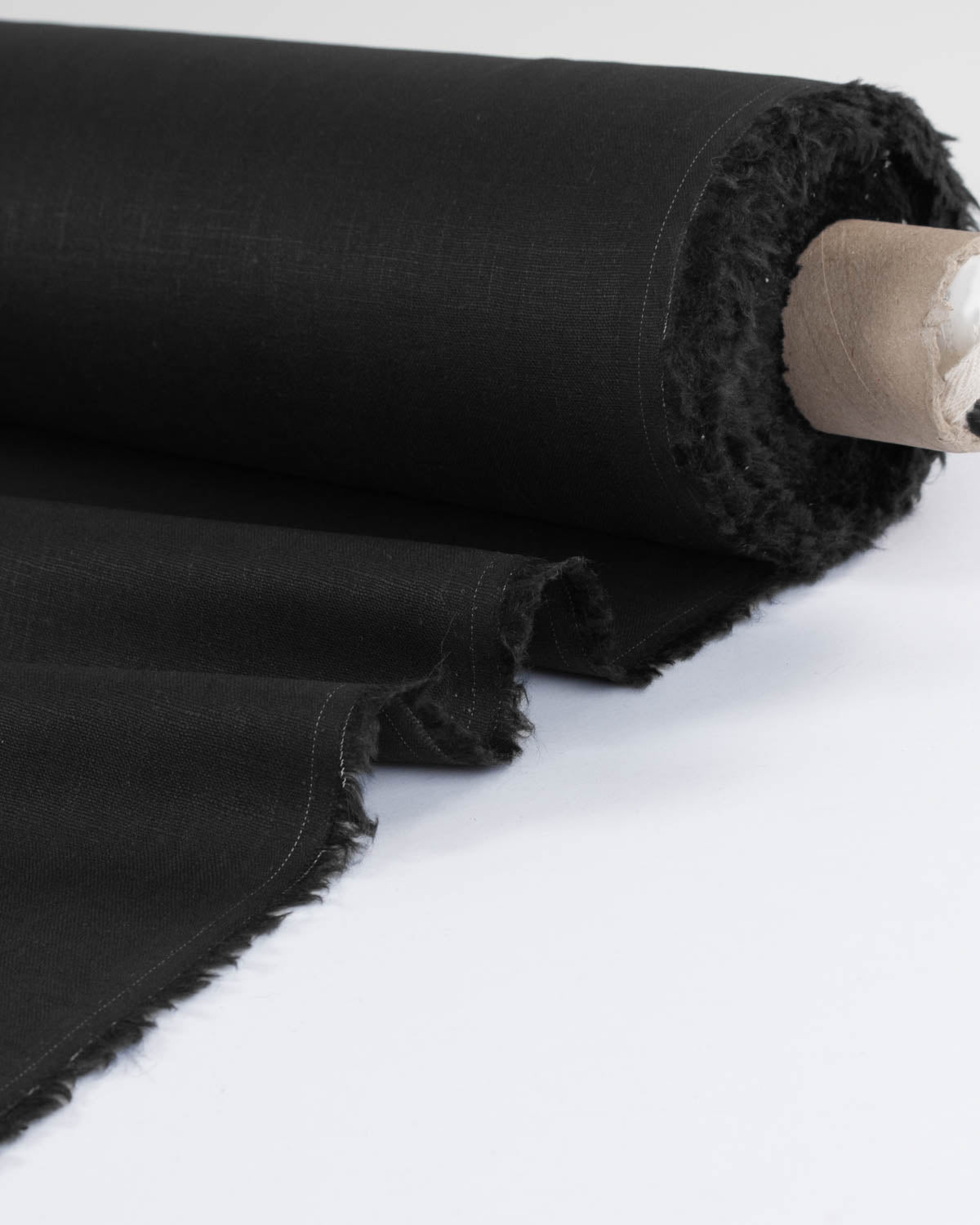 A close-up of a black washed linen fabric roll with frayed edges, partially unrolled on a clean white background.