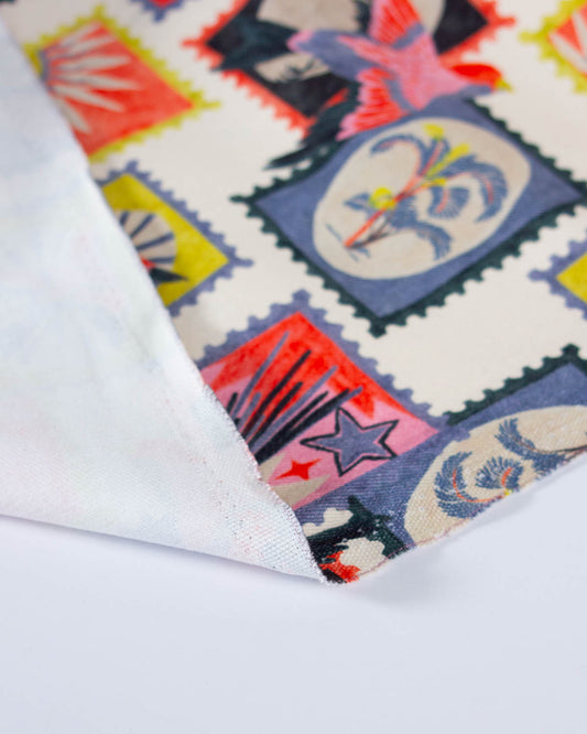 A close-up of a folded white fabric with a colorful printed pattern of postage stamps, showing the texture of the woven material.