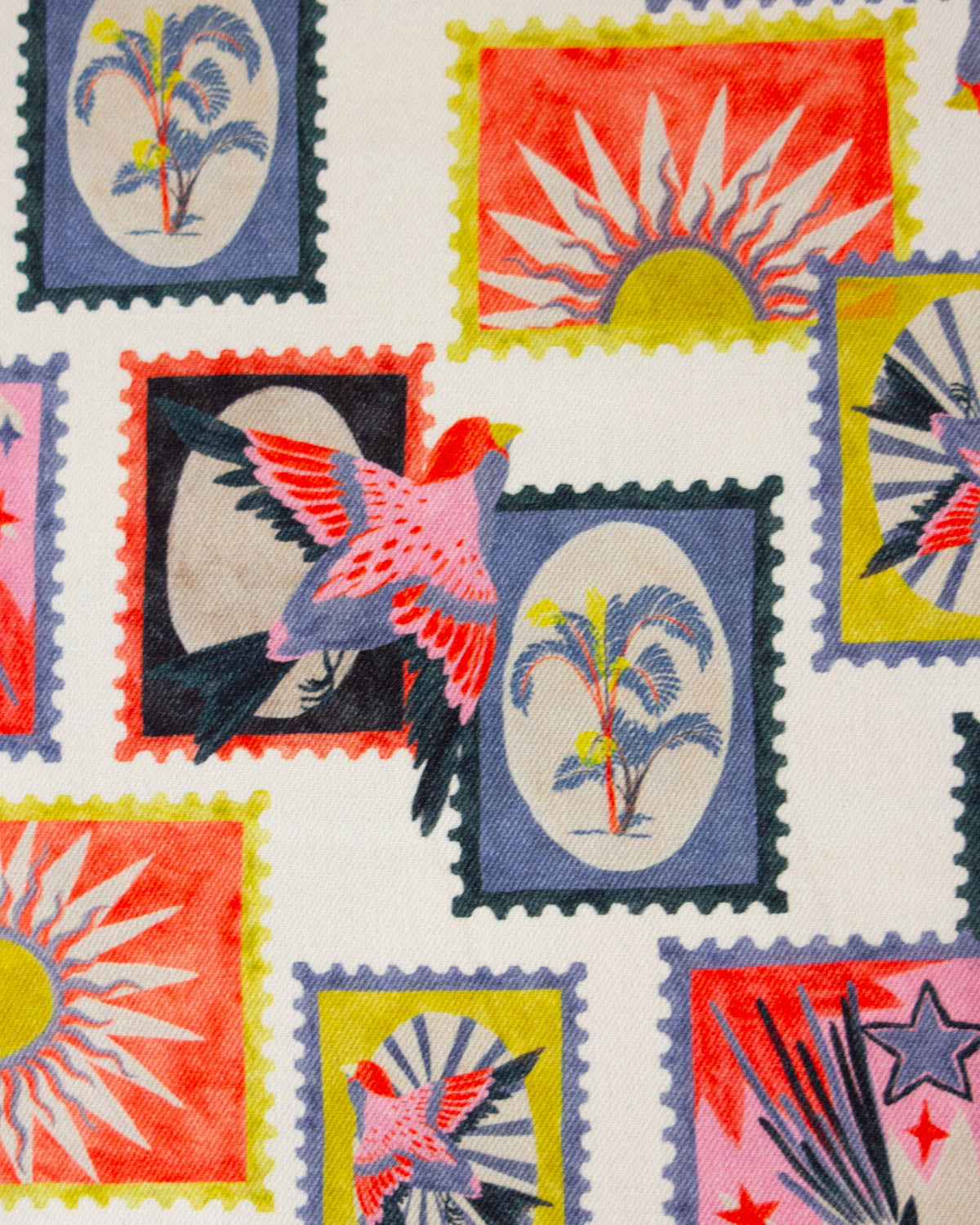 A close-up of a cotton denim fabric or  featuring colorful postage stamp designs with tropical birds, palm trees, suns, and stars on a white background.