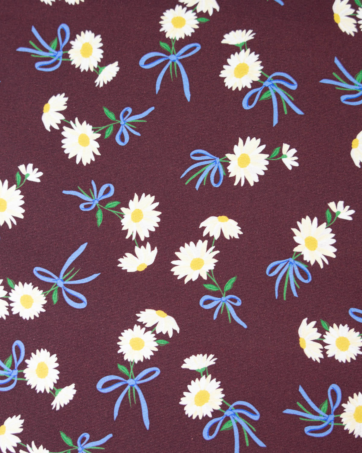 A close-up of a cotton canvas fabric featuring white daisies with yellow centers, scattered blue ribbon bows, and small green leaves on a dark plum-purple background.