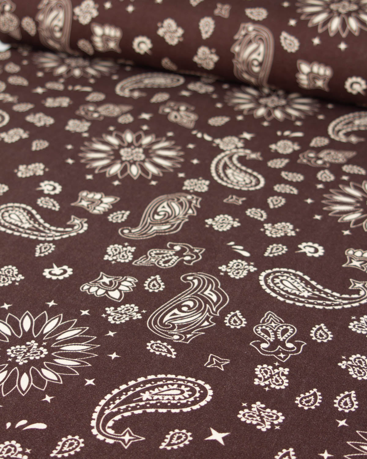 Brown cotton denim fabric with a white paisley and floral bandana print, shown with a rolled section at the top.