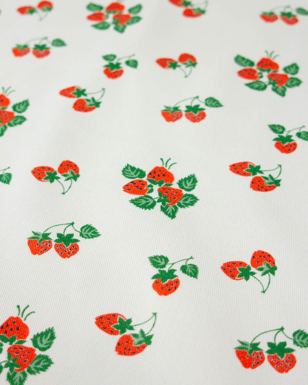 White cotton denim fabric with a repeating pattern of red strawberries and green leaves.