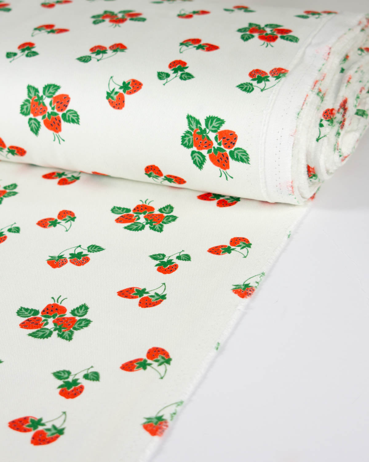 A roll of white cotton denim fabric printed with a repeating pattern of red strawberries and green leaves, shown on a clean white background.