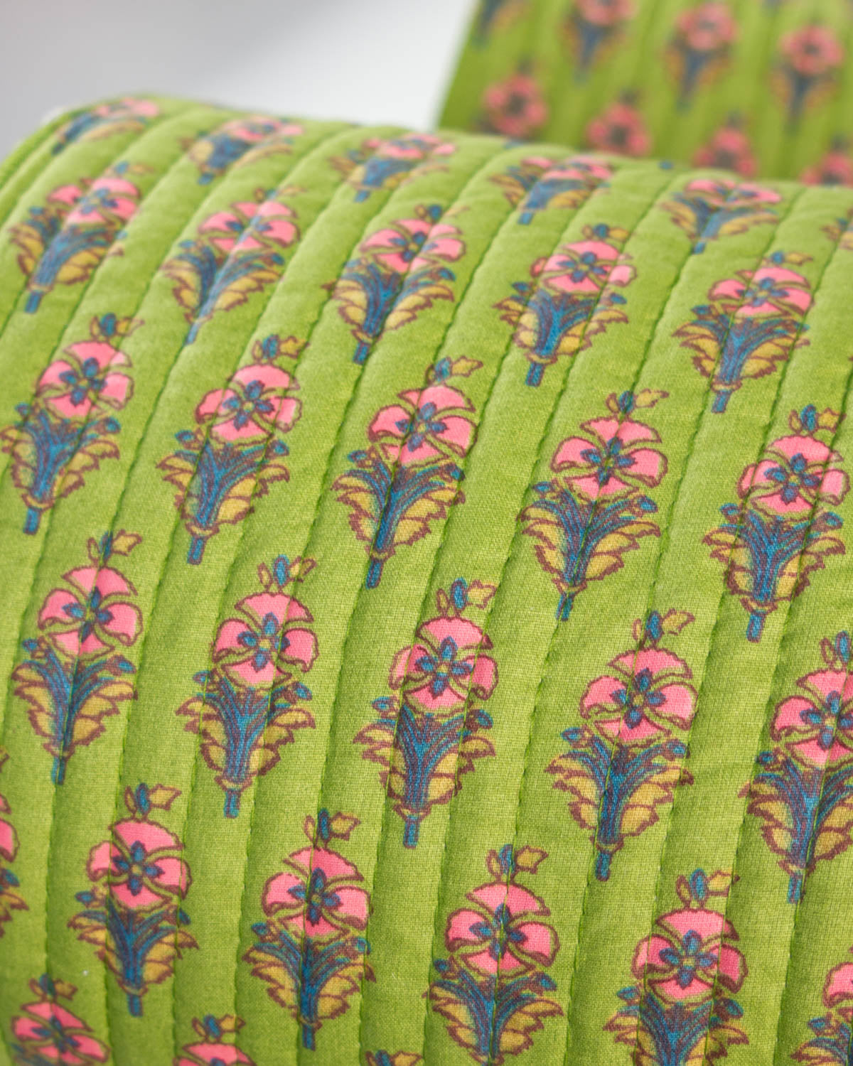 A close-up of a quilted cotton fabric in bright lime green, featuring a repeating floral pattern with pink flowers and blue and yellow-green stems.