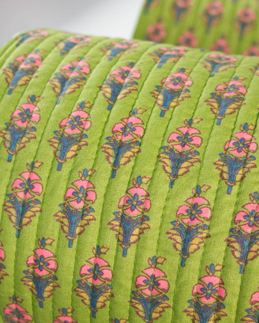 A close-up of a quilted cotton fabric in bright lime green, featuring a repeating floral pattern with pink flowers and blue and yellow-green stems.