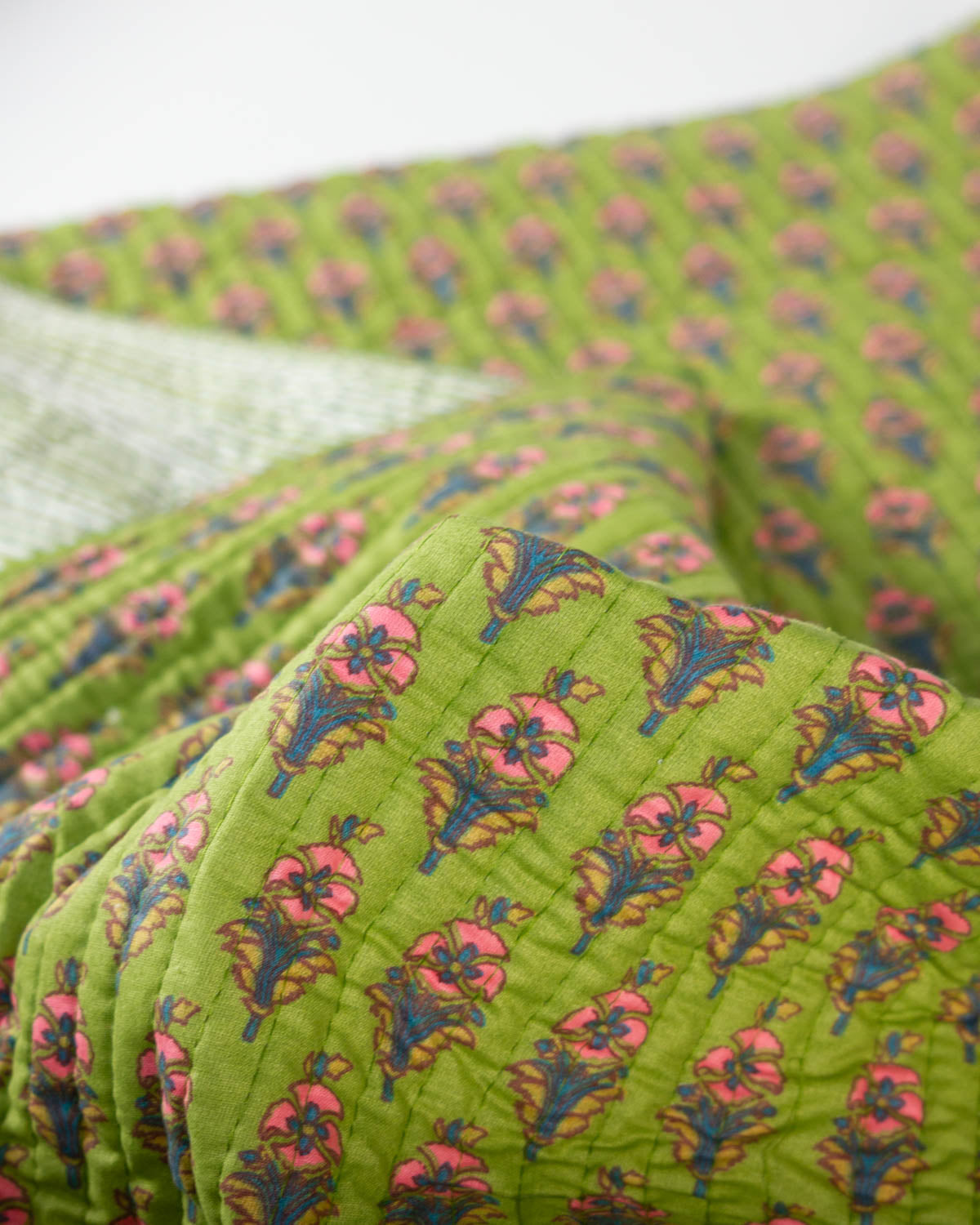 A close-up of a quilted cotton fabric with a lime green background and a repeating floral block print in pink, blue, and yellow.
