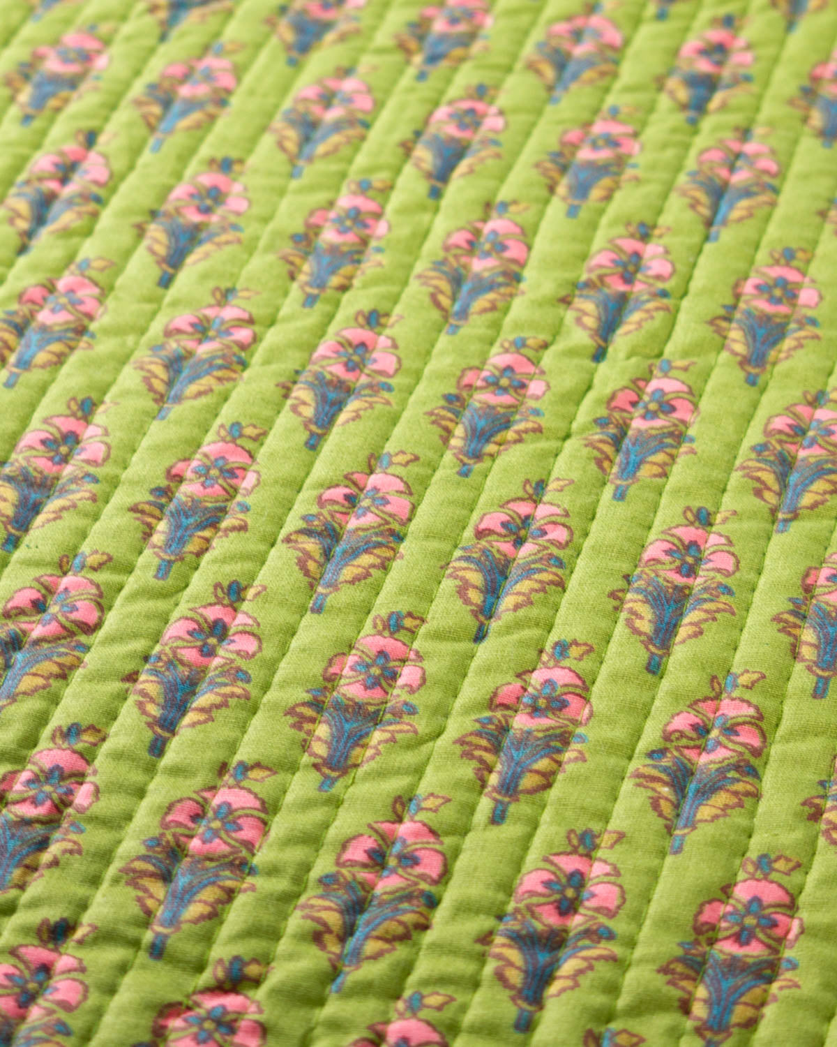 A close-up of a quilted cotton fabric featuring a repeating floral pattern with pink flowers and blue-green leaves on a bright lime green background.